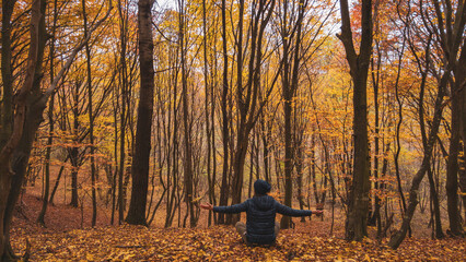 A man sitting calmly in a meditation position on the colorful leaves of the wild forest