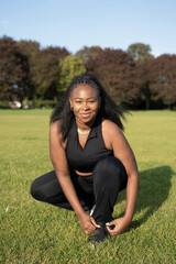 Portrait of young woman tying shoes before exercising in park - obrazy, fototapety, plakaty