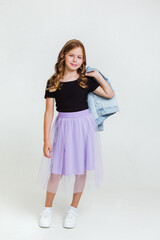 cheerful preteen girl in black t-shirt, violet skirt and white sneakers posing and standing on white background