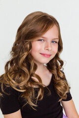 Close-up portrait of cute blonde curly kid girl in black t-shirt on white studio background.