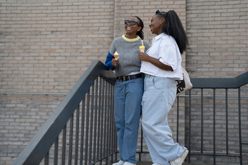 Young female friends eating ice cream on staircase