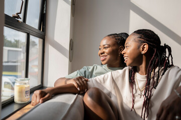 Portrait of happy lesbian couple looking through window at home