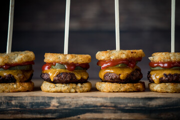 A row of tater beef slider skewers on a wooden board, against a dark background.