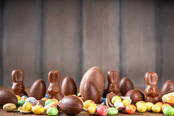 Easter background greeting card with holiday traditional confectionery, Easter egg hunt fun concept. Chocolate bunny, chocolate and candy Easter eggs on wooden background