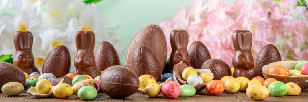 Easter background greeting card with holiday traditional confectionery, Easter egg hunt fun concept. Chocolate bunny, chocolate and candy Easter eggs on wooden background