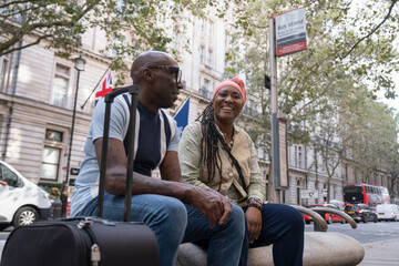 UK, London, Happy mature couple sitting at bus stop - obrazy, fototapety, plakaty