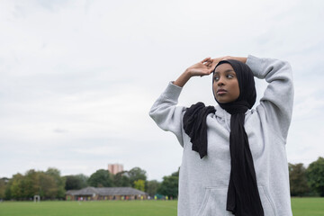 Portrait of woman in hijab standing in soccer field with arms raised