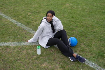 Portrait of pensive woman in hijab sitting in soccer field