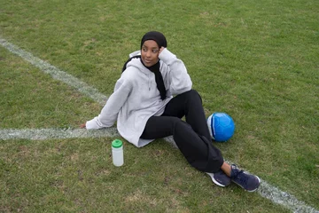Foto op Plexiglas Portrait of pensive woman in hijab sitting in soccer field © Cultura Creative