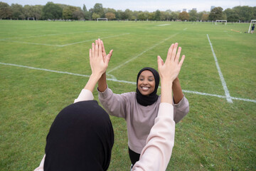 Two smiling women in hijabs giving high five in soccer field