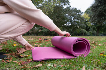 Close-up of woman unrolling yoga mat on grass in park - obrazy, fototapety, plakaty