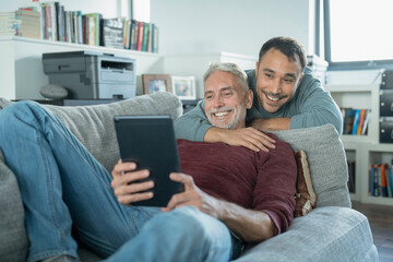 Smiling male couple using digital tablet on sofa