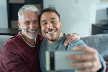 Smiling male couple taking selfie on sofa