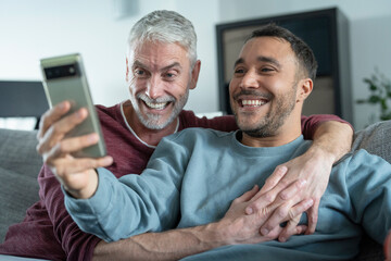 Smiling male couple taking selfie on sofa