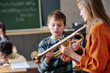 Selective focus medium shot of young female teacher giving trumpet to boy during music class © AnnaStills