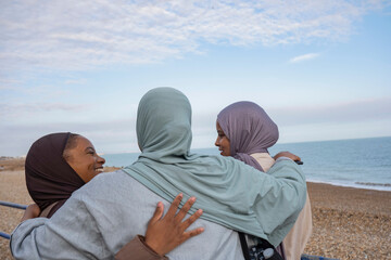 Three Muslim friends embracing on beach