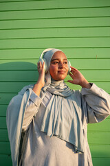 Portrait of Muslim woman listening to music against green wall