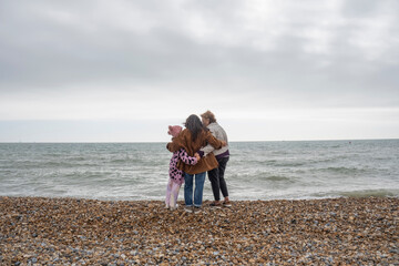 Grandmother, mother and daughter embracing on beach on cloudy day