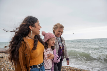 Grandmother, mother and daughter walking on beach on cloudy day
