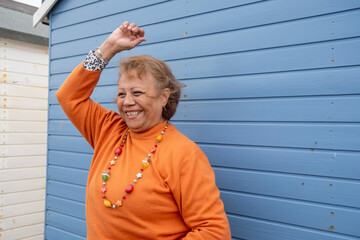 Portrait of smiling senior woman with hand raised against blue hut