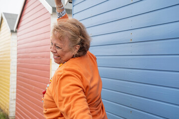 Side view of smiling senior woman with hand raised against beach hut