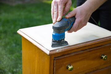 Person using a grinder removes old paint from furniture, restoration of antique furniture