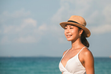 Portrait of smiling young Asian woman wearing a straw hat standing at the beach on vacation.