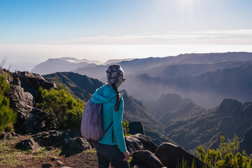 Hiker woman with scenic view of misty hills and canyon of rugged terrain on Madeira island,...
