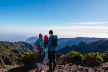 Fototapeta premium Hiker family with small child looking at scenic view of misty hills and canyon of rugged terrain on Madeira island, Portugal, Europe. Idyllic hiking trail to mountain peak Pico Ruivo. Aerial vista