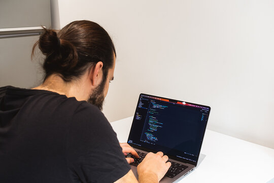 Young professional software engineer, IT specialist, programmer, working at home and writing code on a laptop computer. A programmer works remotely at home on his laptop.