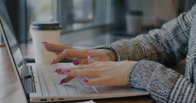 Close-up of female hands typing with laptop computer while businesswoman working at table in cafe. Business and freelance job concept.