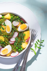 Hot spring salad with asparagus, boiled potatoes, radishes, fresh green peas, and farm eggs. Fresh spring recipes with asparagus, balanced healthy food