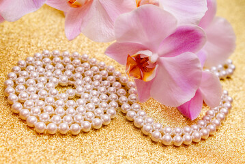 purple Orchid and pearl necklace on a shiny gold background
