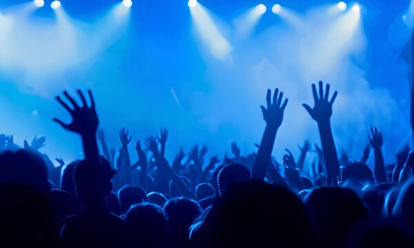 Concert audience with raised hands against a stage with blue lighting. The concept of a live concert and music event.