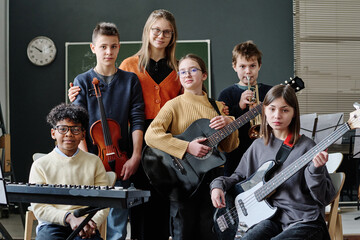 Group portrait of modern middle school orchestra members and music teacher posing for camera with...