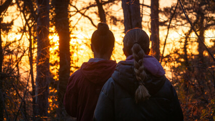 Two young white women walking in the woods at sunset, one of them with a braid on her hair