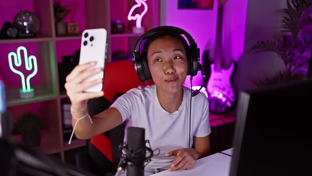 Asian woman making a selfie in a neon-lit gaming room at night
