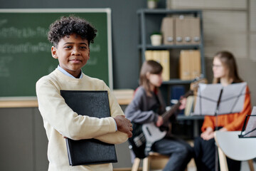 African American boy holding sheet music in folder standing in classroom, his classmate with bass...