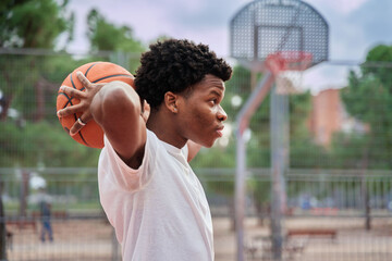 Young basketball player in his early twenties posing with the ball held behind his head.
