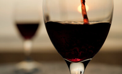 Close up pouring red wine at sunset on seaside view deck landscape. Close-up view of pouring red wine into glass on landscape background.