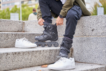 Legs of young man putting on roller skates in the city. unrecognizable man sit with inline skates