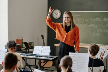 Medium long shot of young Caucasian music teacher directing middle school orchestra, copy space