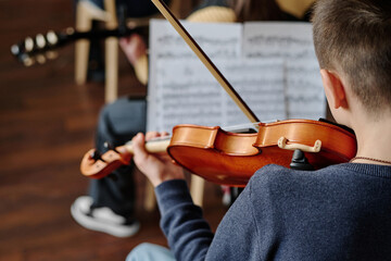 Selective focus rear view shot of unrecognizable teen boy playing violin in school orchestra, copy...