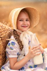 A portrait of a happy girl in a wheat field at sunset. A child holds a glass jar with milk against the background of rye ears.
