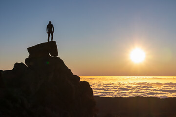 Silhouette of person standing on massive rock watching romantic sunrise on mountain peak Pico do...