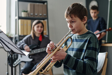 Selective focus shot of Caucasian boy practicing trumpet in modern school orchestra, copy space