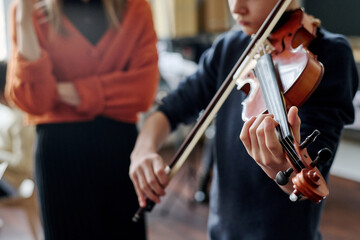 Selective focus shot of Caucasian teen boy learning to play violin at school, his unrecognizable...