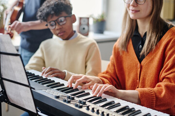 Selective focus shot of of modern young female music teacher playing synthesizer during class, her...