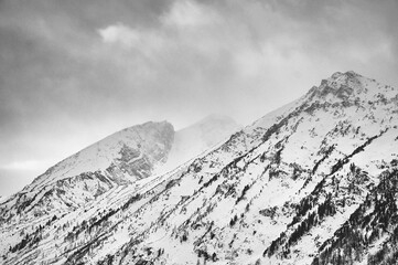 Sunlight breaks through clouds above snowcovered mountains.