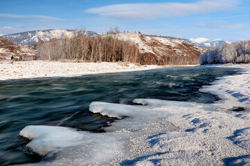 A frozen river bank with a distant mountain under a cloudy sky